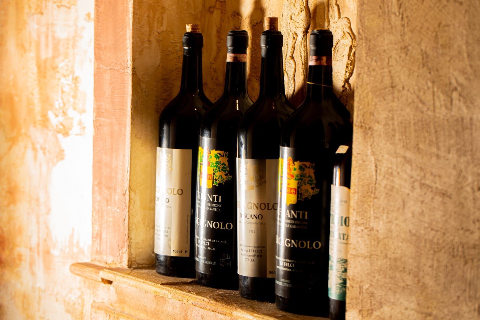 Quattro bottiglie di vino sono allineate su uno scaffale contro il muro.