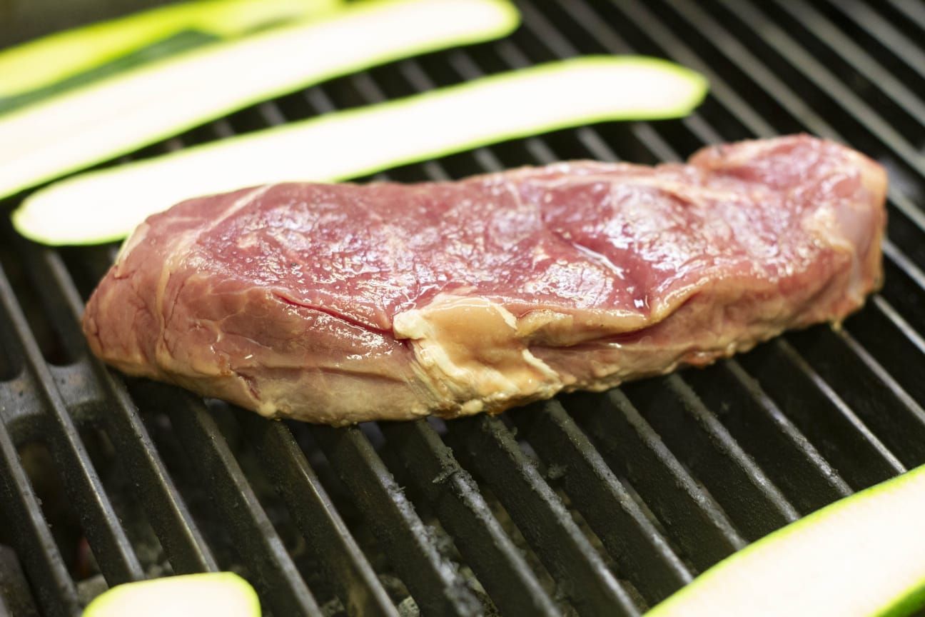 Una bistecca sta cuocendo su una griglia accanto alle zucchine