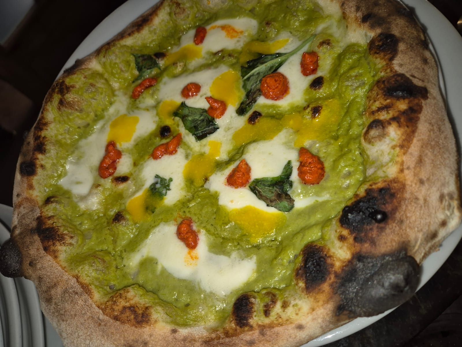 Una pizza con salsa verde e pomodori su un piatto bianco