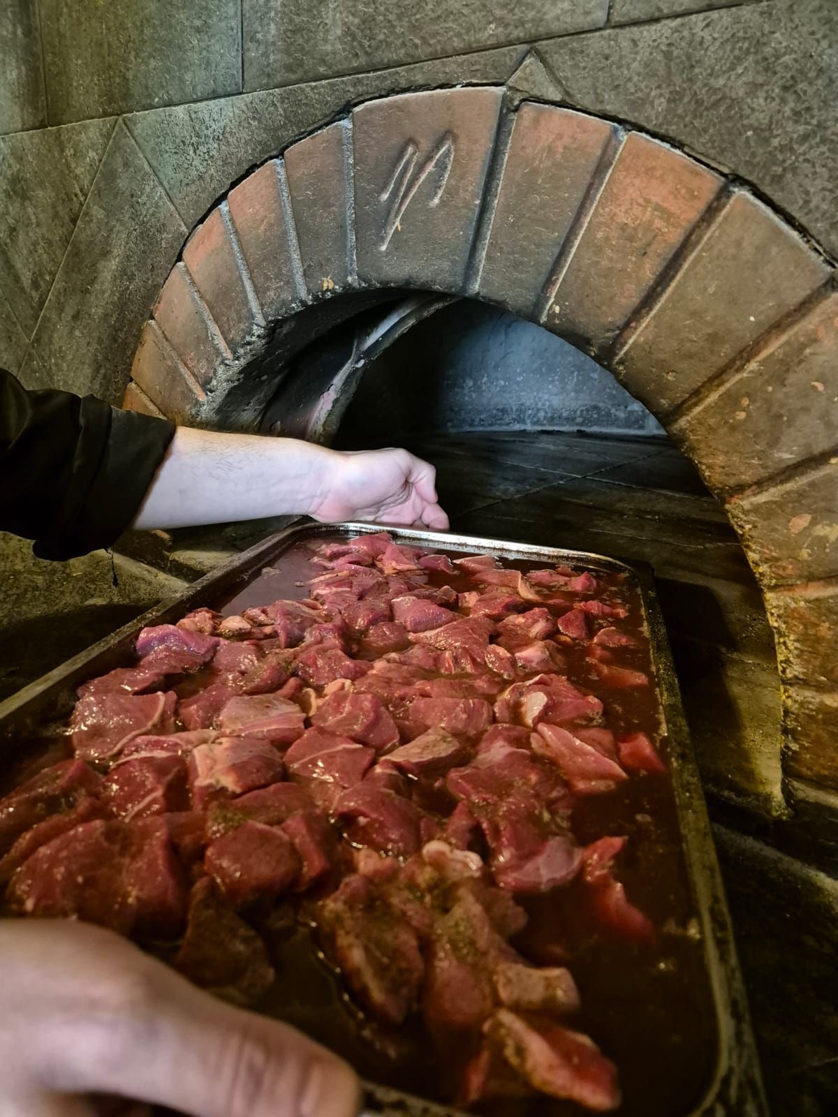 Una persona sta mettendo la carne in un forno di mattoni