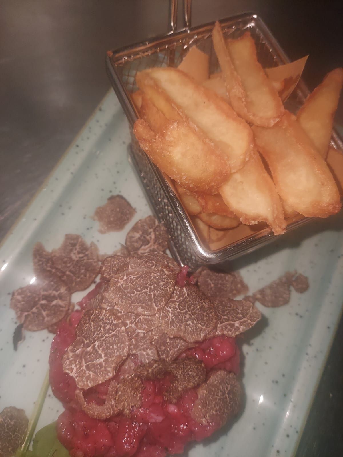 C'è un cestino di patatine fritte accanto a un piatto di cibo.