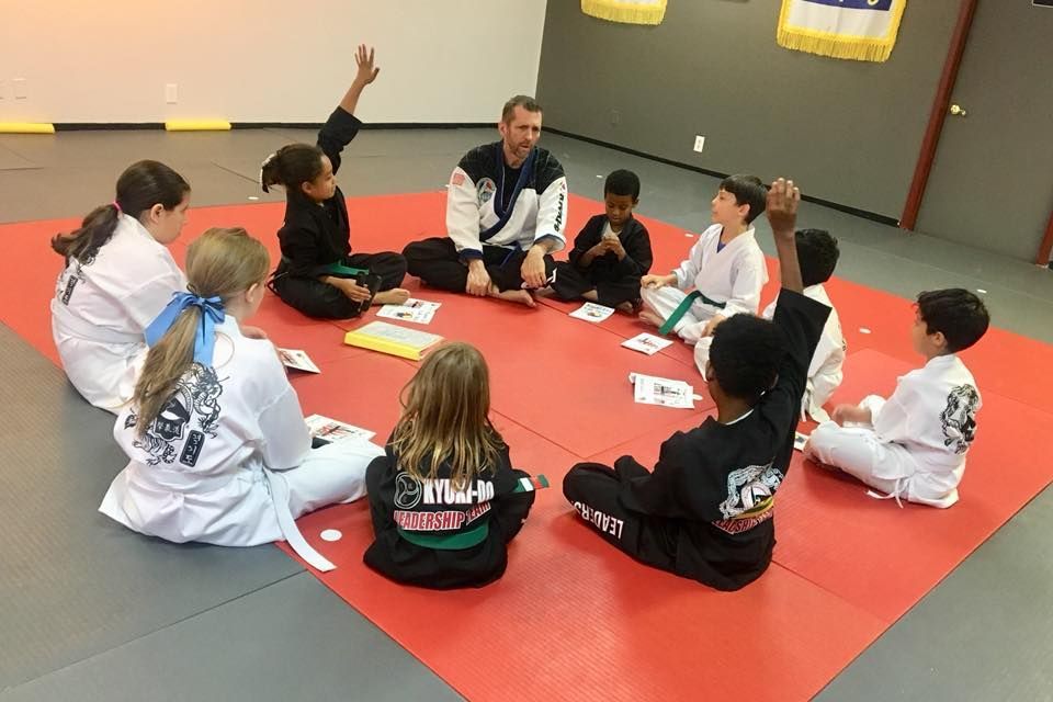 a group of kids are sitting in a circle on a red mat