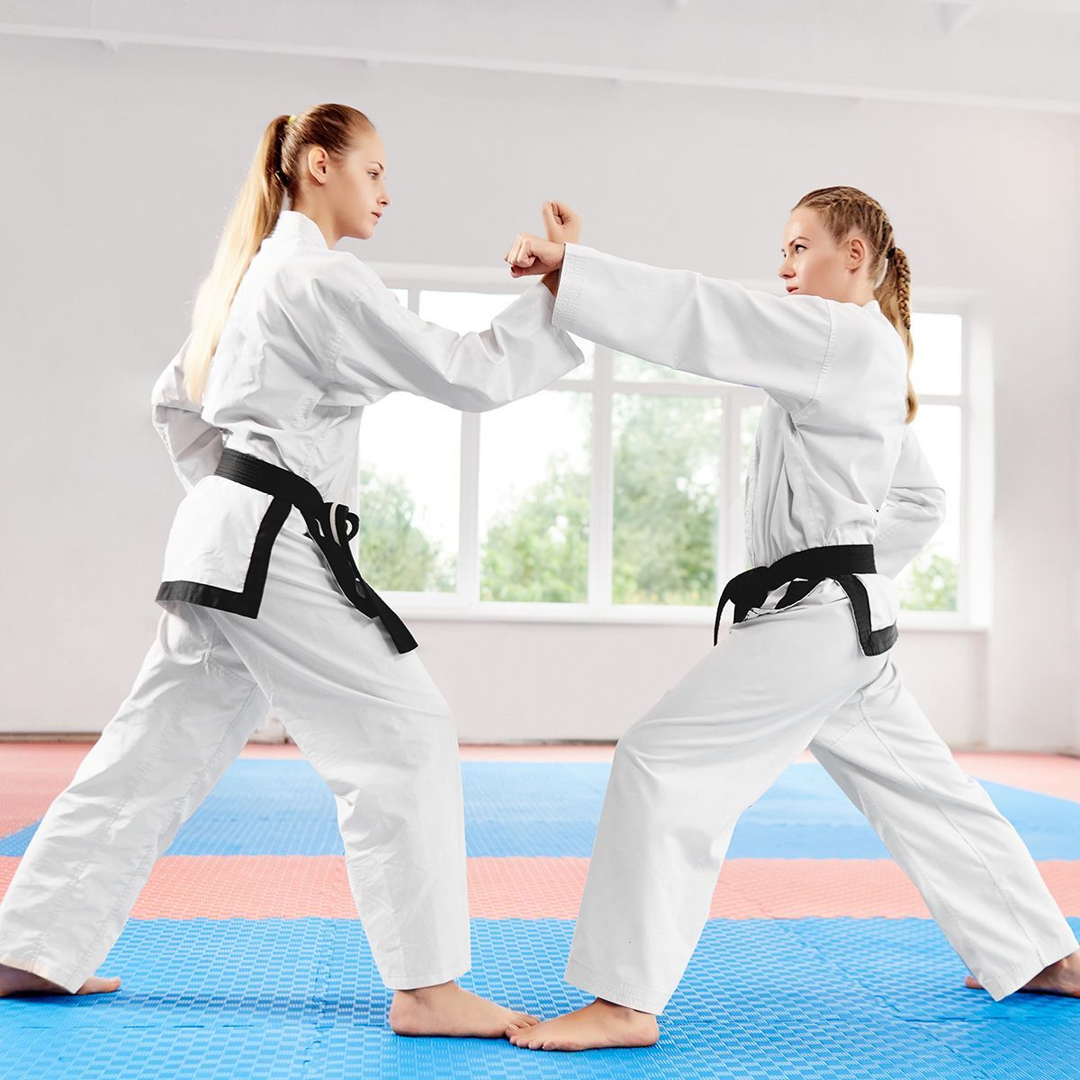 two women are practicing karate on a mat in a gym .