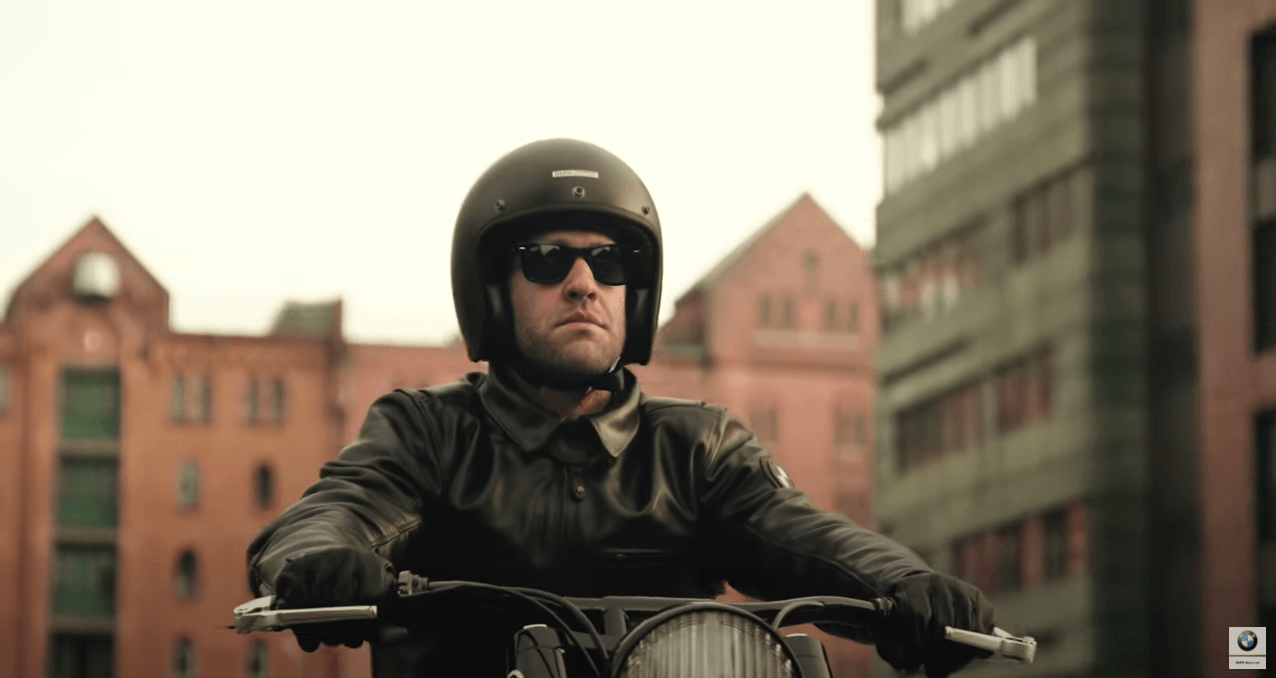 Ein Mann mit Helm und Sonnenbrille fährt in einer Stadt Motorrad.