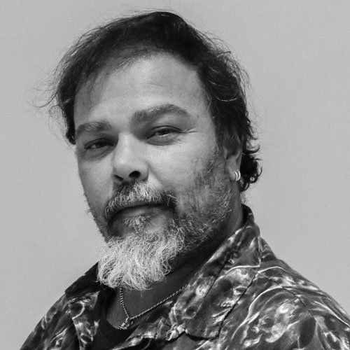 Man with graying beard and patterned shirt, looking towards the camera.
