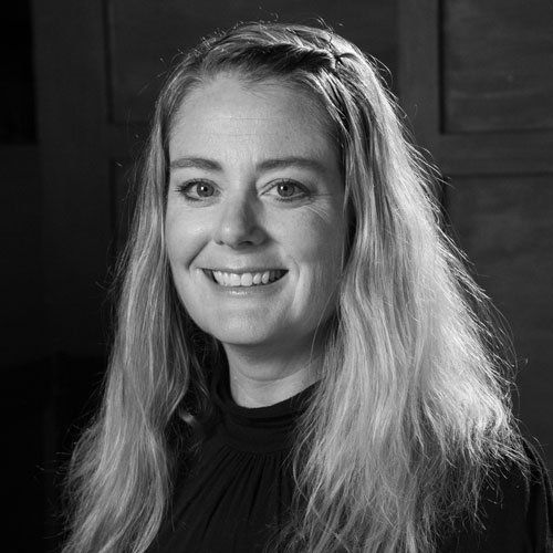 Woman with long blonde hair smiles, braided across the top. Wearing a black top.