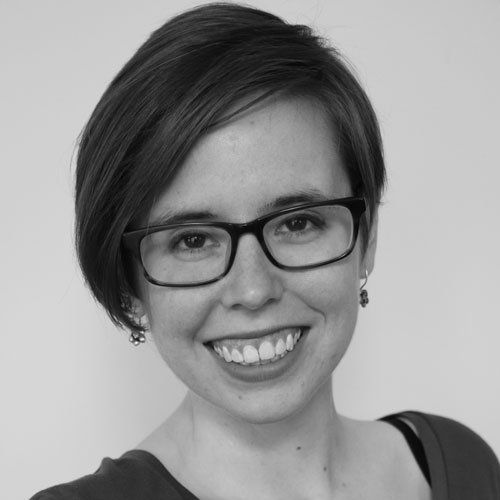 Woman with short hair, glasses, and a wide smile, in a black and white photo.