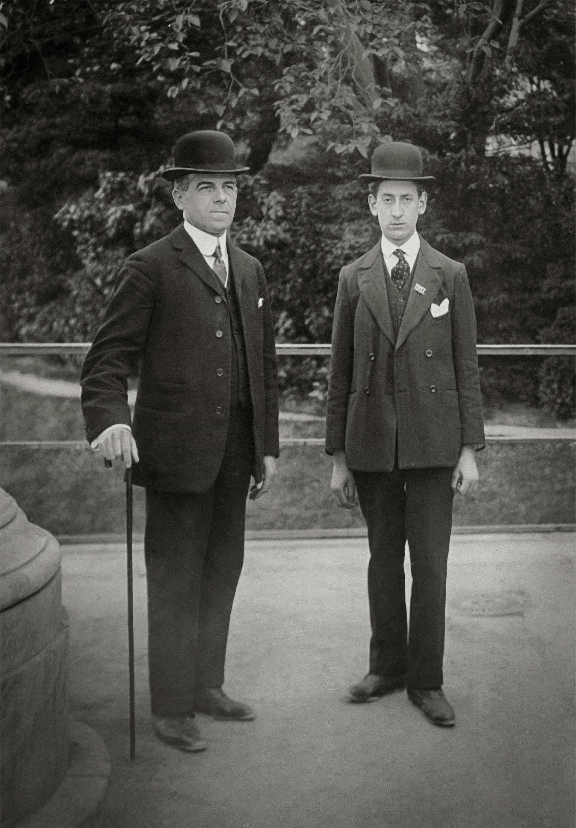 Two men in suits and hats are standing next to each other