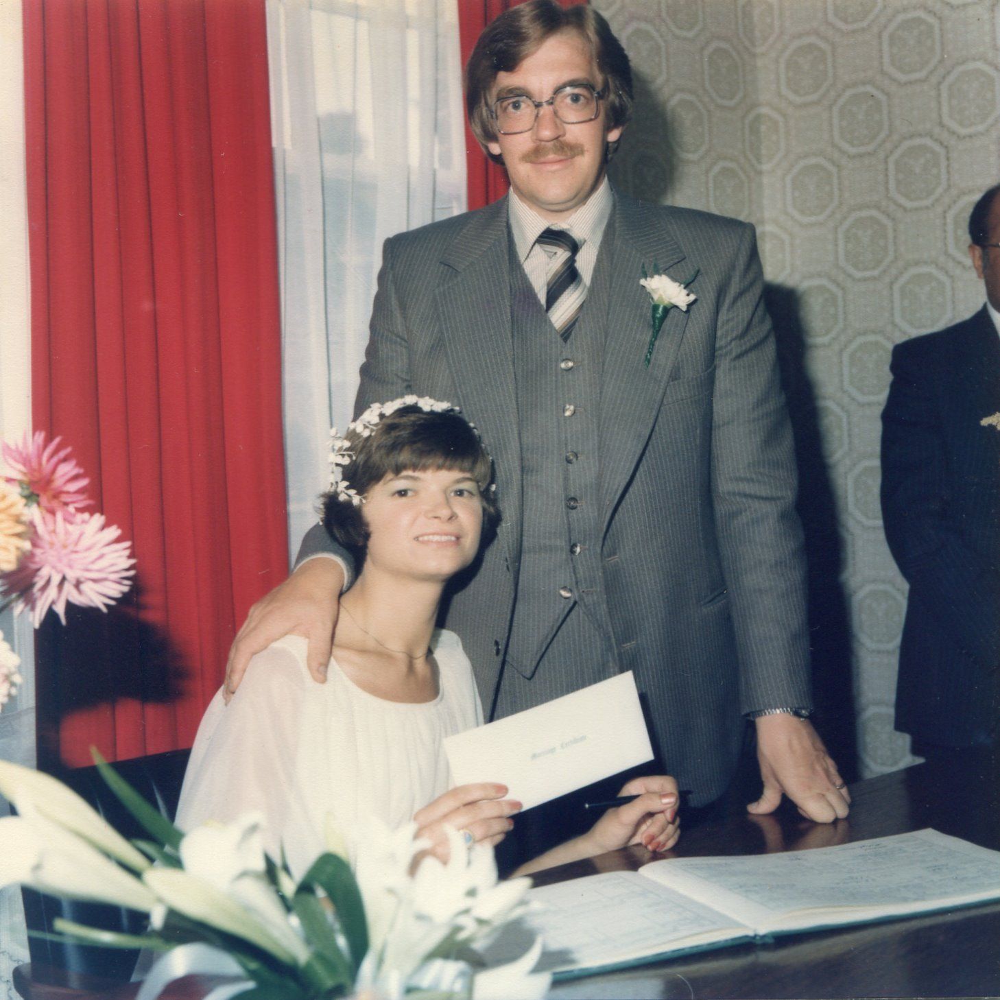 A man in a suit stands next to a woman in a white dress