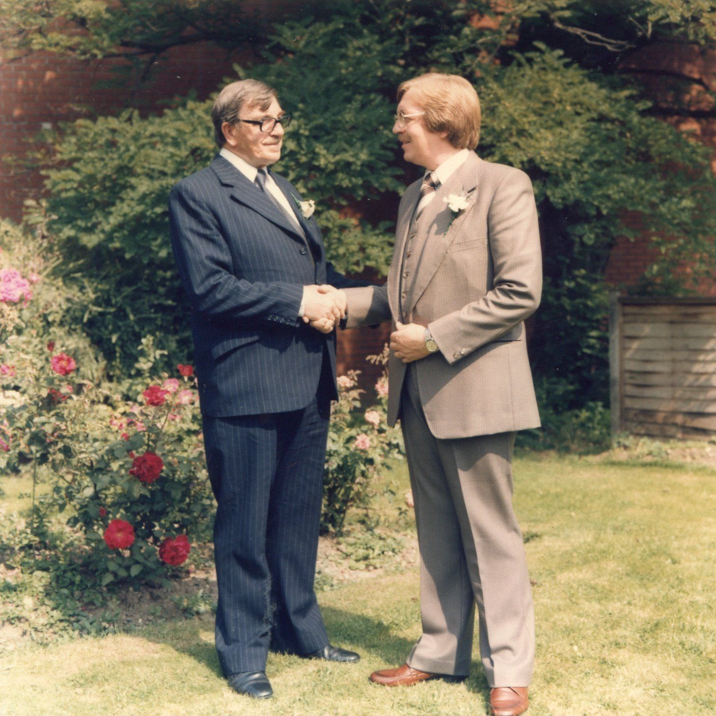 Two men in suits shaking hands in a garden