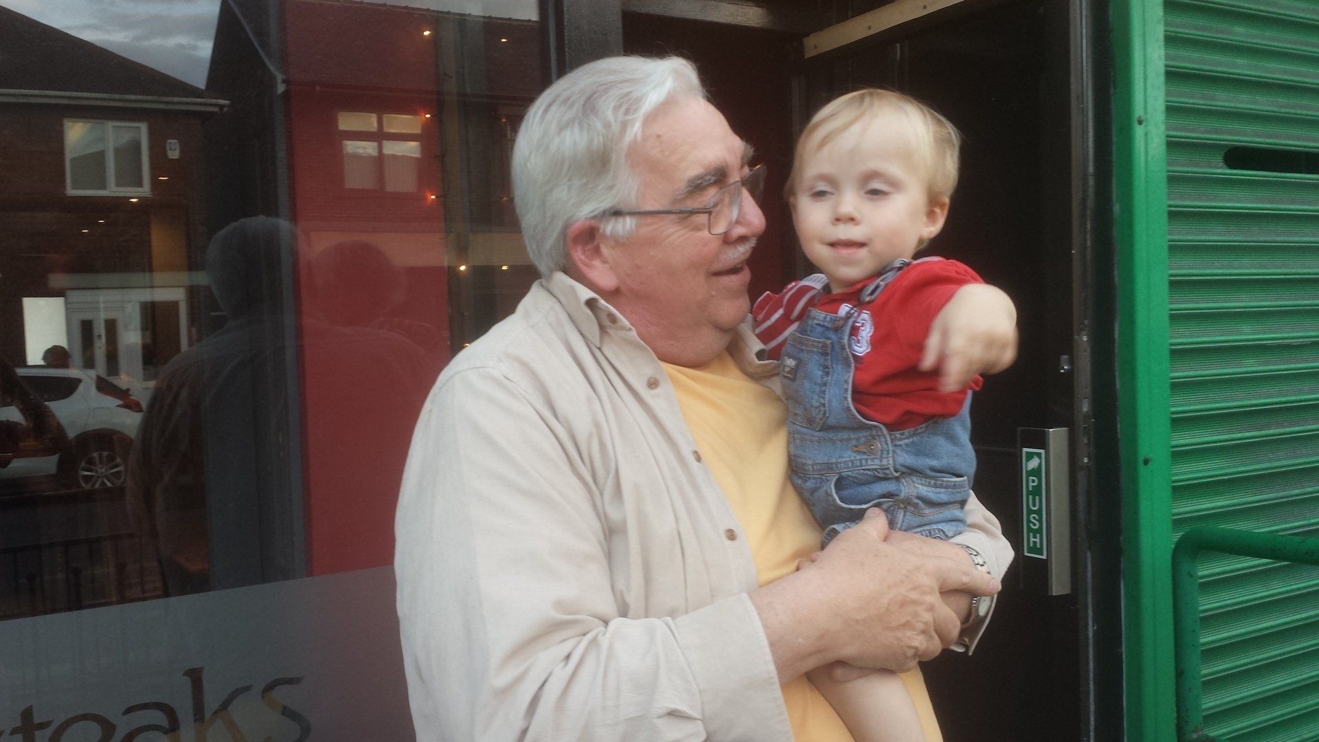 A man is holding a baby in his arms in front of a green door.
