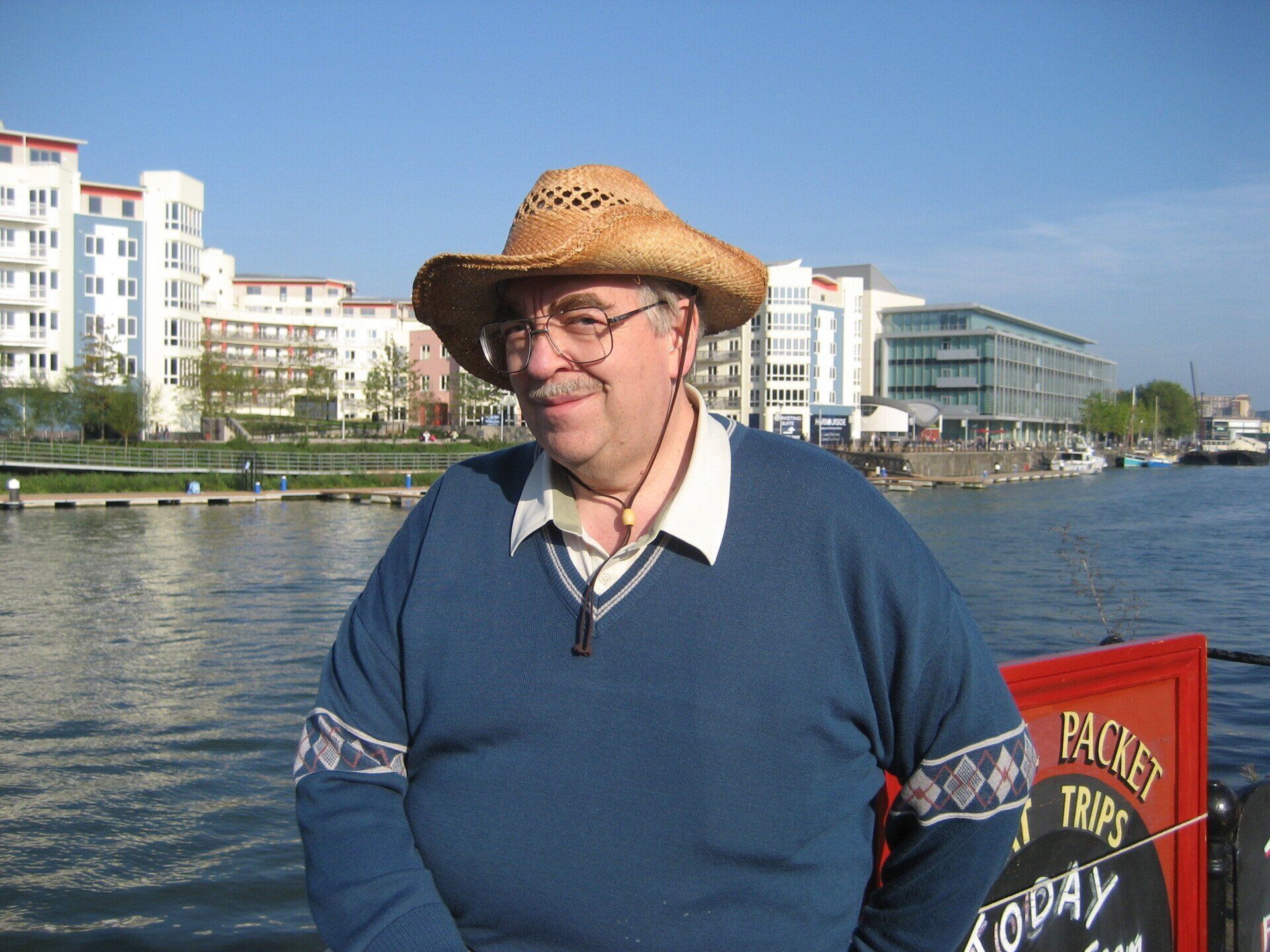 A man wearing a cowboy hat and a blue sweater stands in front of a sign that says today
