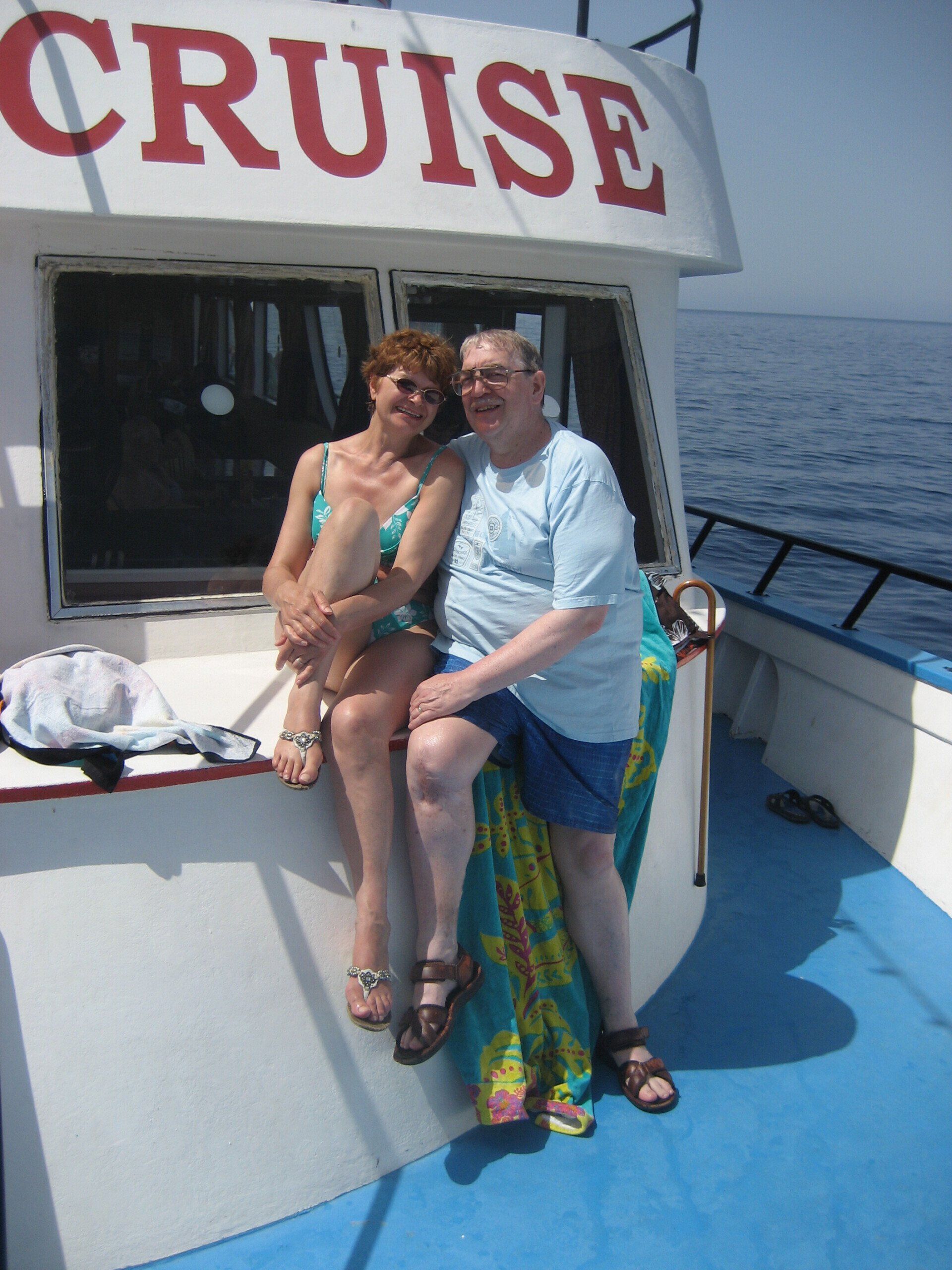 A man and a woman sit on the side of a cruise boat