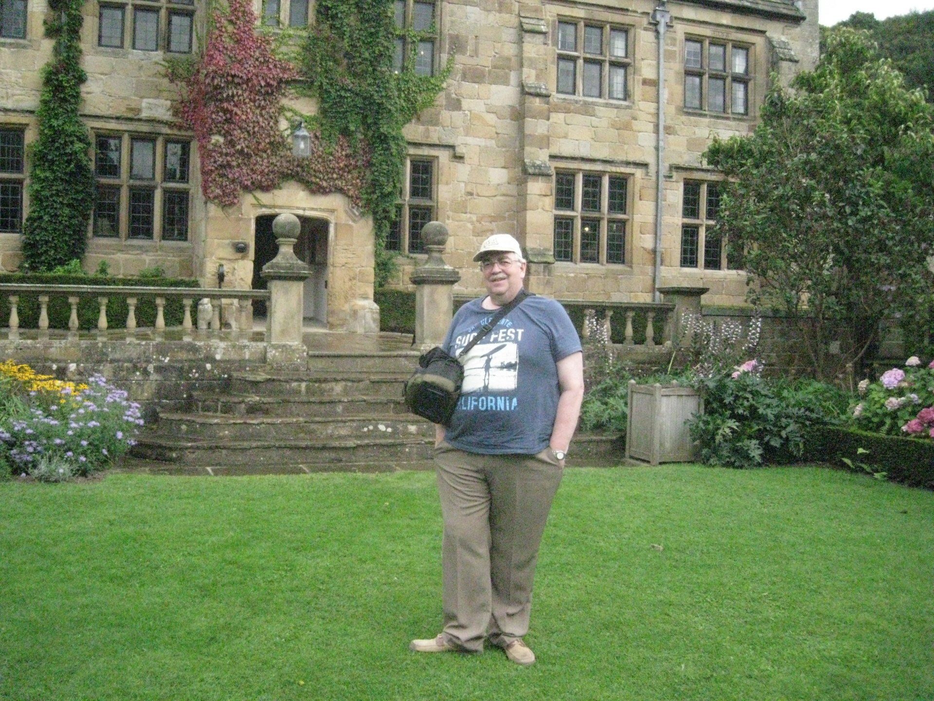 A man in a blue shirt is standing in front of a large stone building.