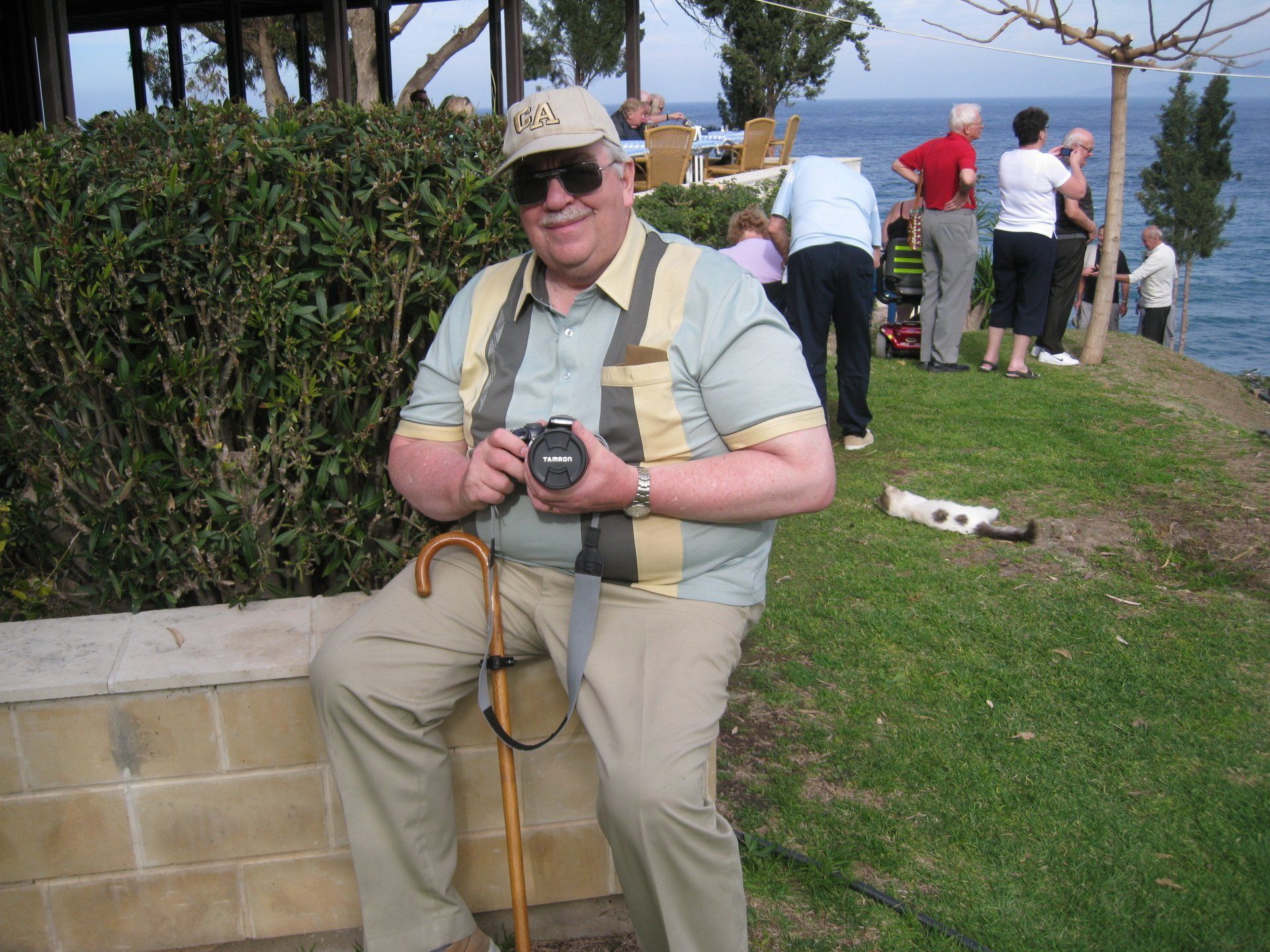 A man sitting on a wall holding a camera and a cane