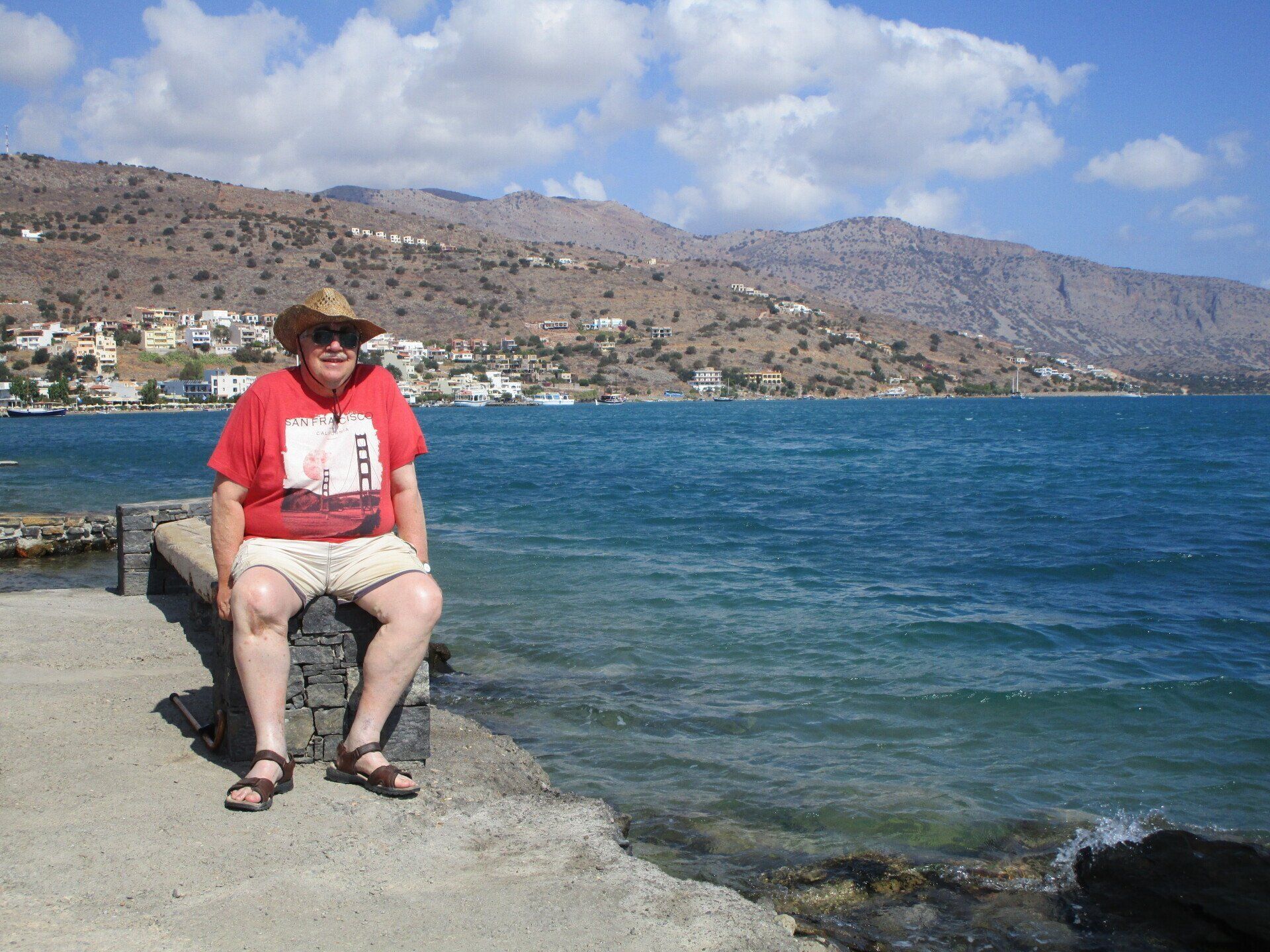 A man in a red shirt is sitting on a rock near the water