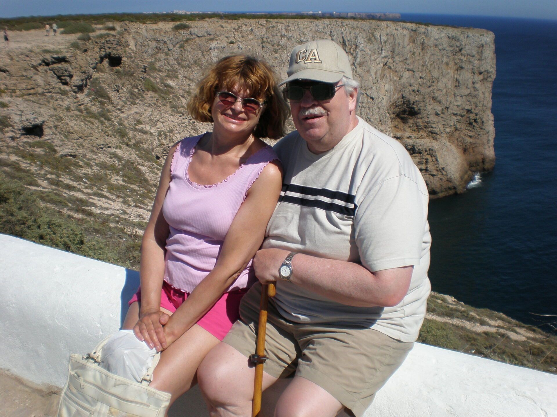 A man and a woman are posing for a picture in front of a cliff overlooking the ocean