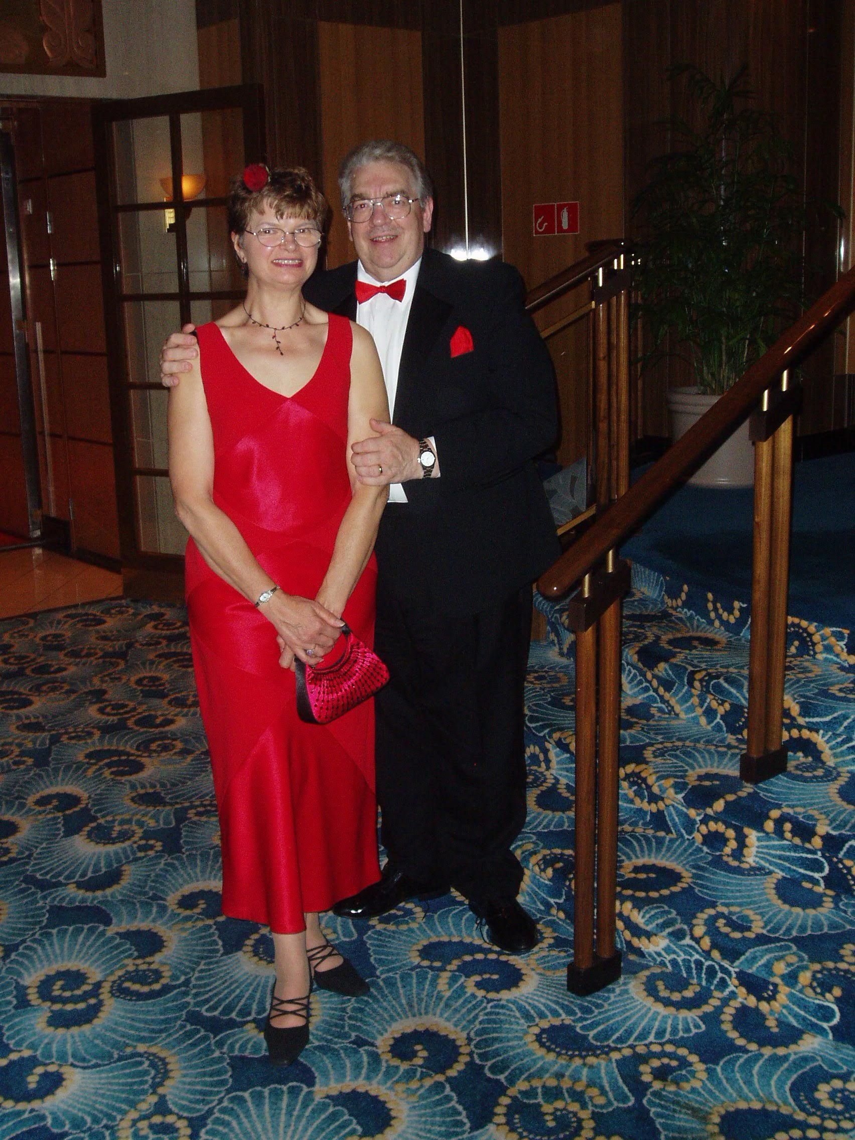 A man in a tuxedo stands next to a woman in a red dress