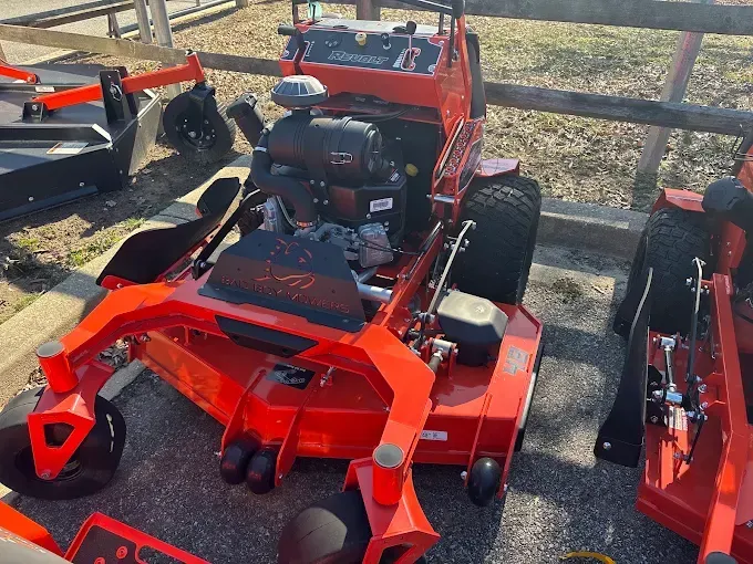 Red riding lawn mower displayed outdoors beside another mower on a paved lot.