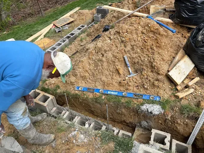 Worker near cinder block foundation trench on a muddy construction site