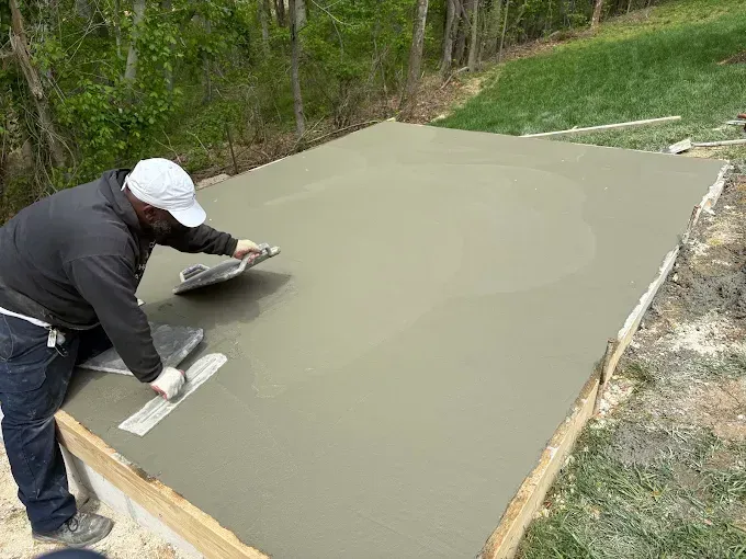 Worker smoothing fresh concrete on a large slab outdoors.
