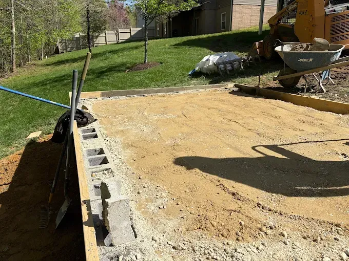 Fresh concrete slab being finished beside cinder blocks and a wheelbarrow at a construction site