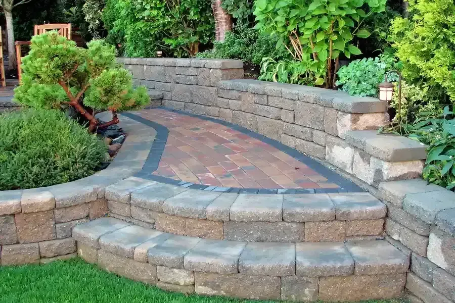 Curved stone patio with pavers, steps, and lush green landscaping in a garden