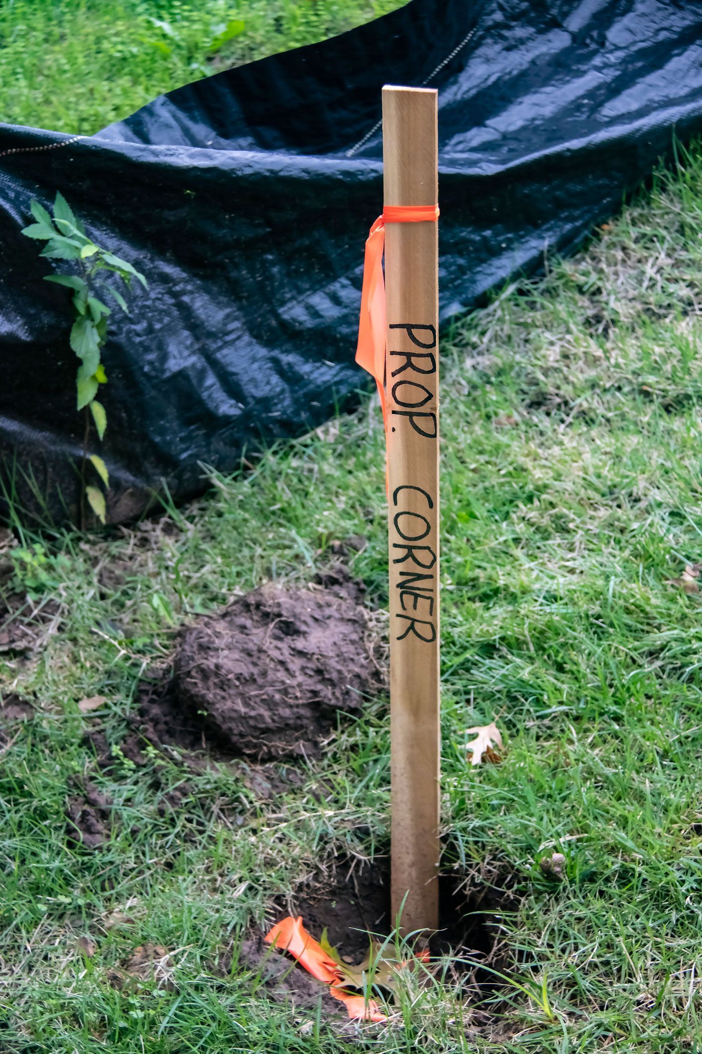 Closeup of wooden stake in ground with orange tape and Property Corner marked on it near construction barrier made of heavy black plastic
