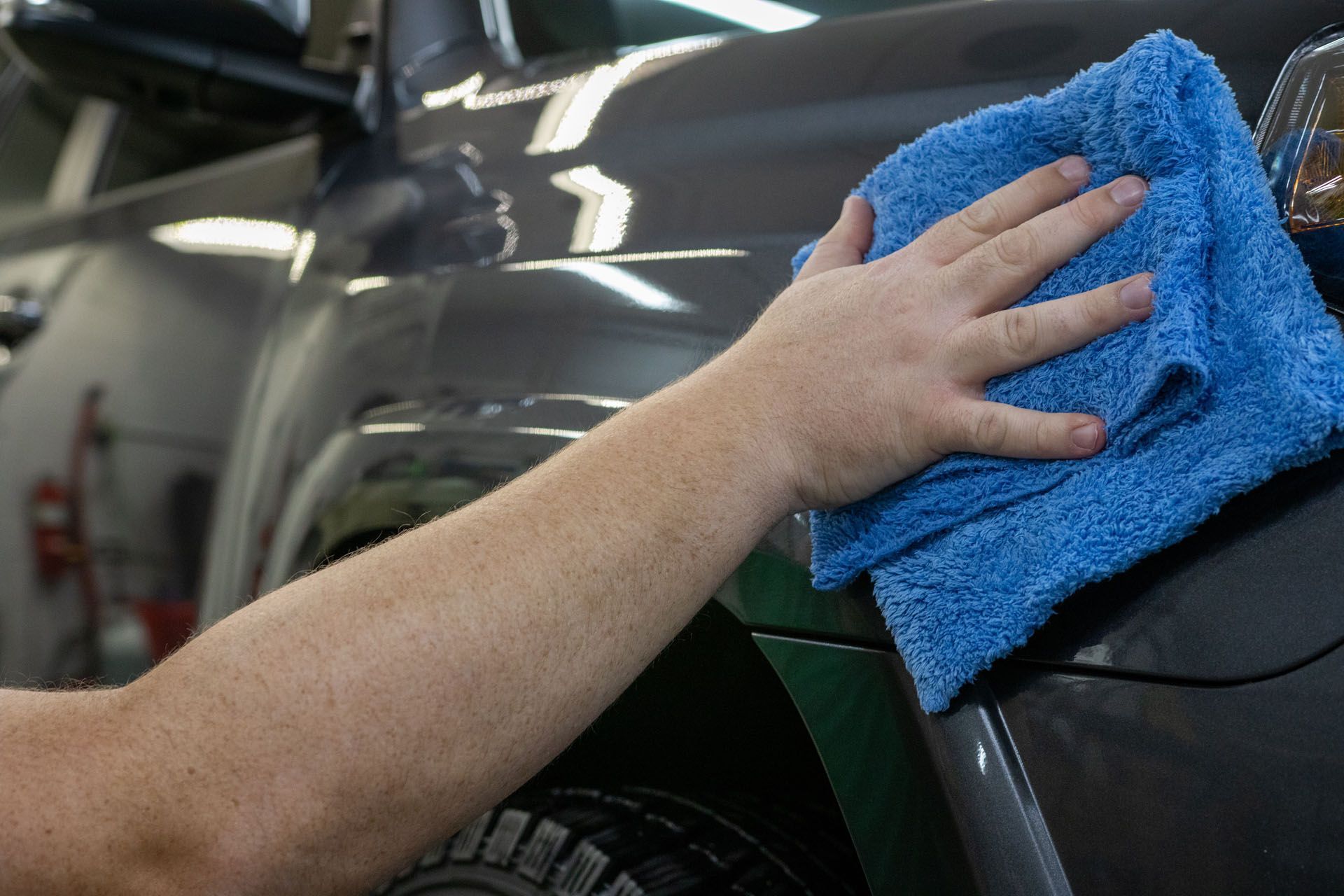 Person wiping down a dark gray car with a blue microfiber cloth.