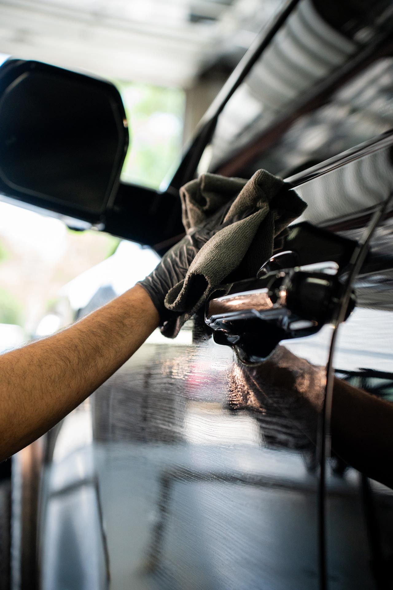 Person wearing gloves wiping down a black car's door with a cloth.