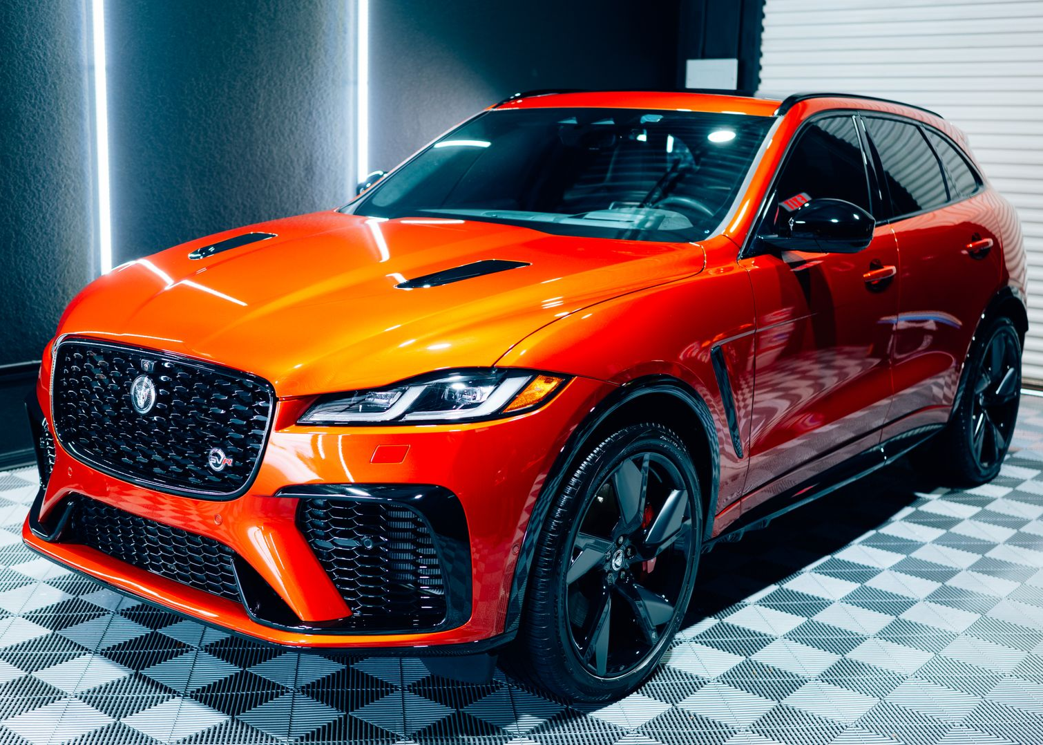 Orange Jaguar F-PACE SUV parked indoors, featuring black accents and wheels, under bright lights.