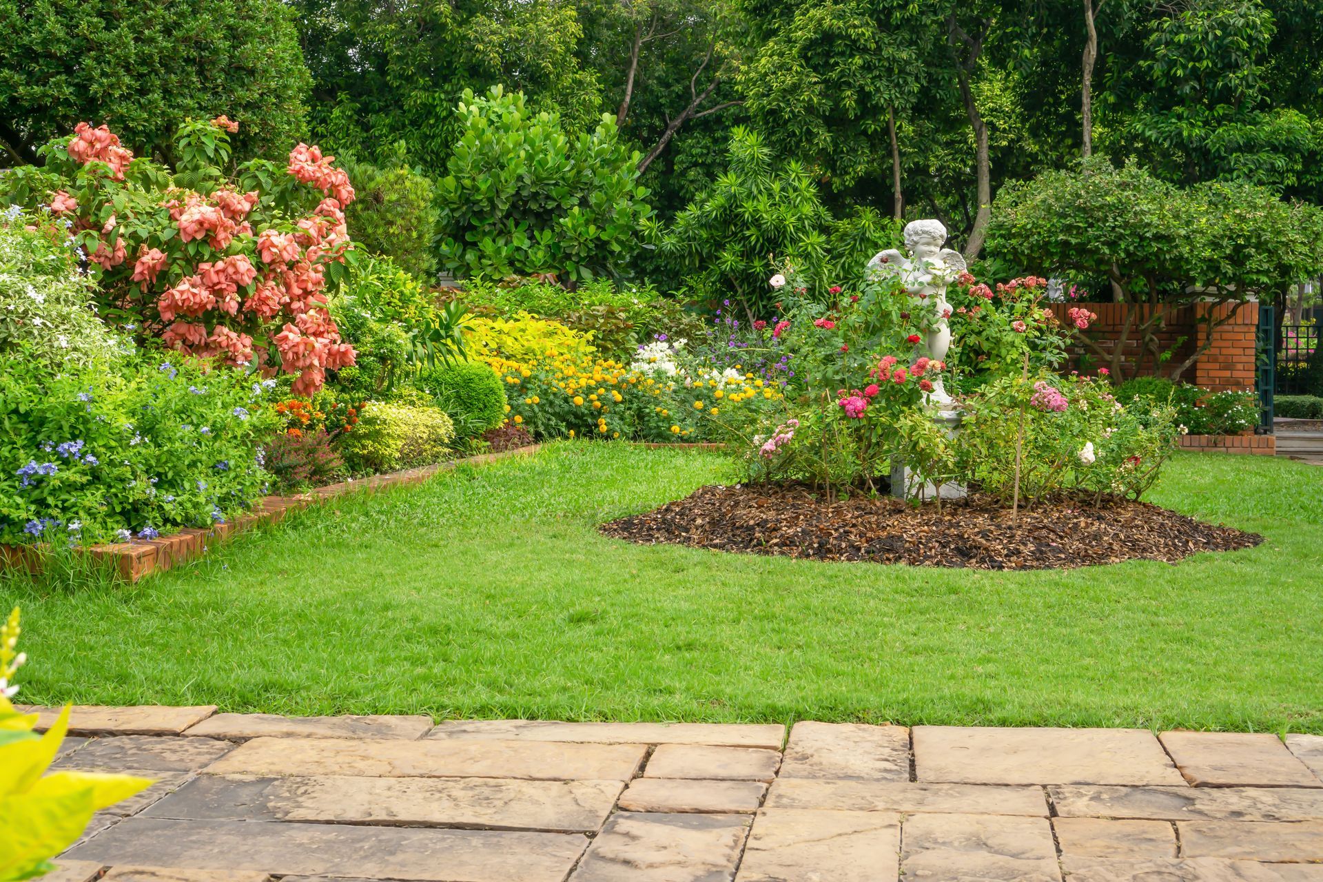 Vibrant garden scene featuring a variety of colorful flowers blooming on a brown pavement, bordered by a lush green lawn.