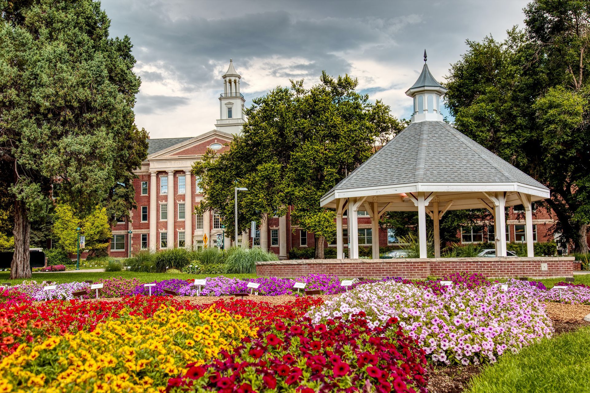 An assortment of vibrant flowers in shades of pink, purple, yellow, and red bloom near a charming gazebo.