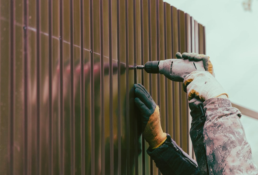 a person is using a drill to install a fence .