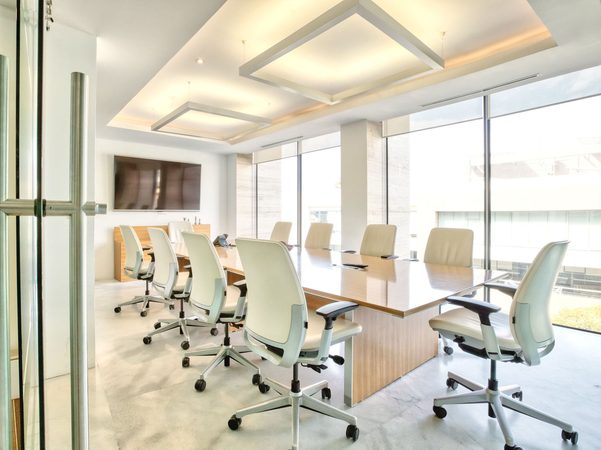 Moderna sala de conferencias de oficina con una mesa grande, sillas blancas y grandes ventanales.
