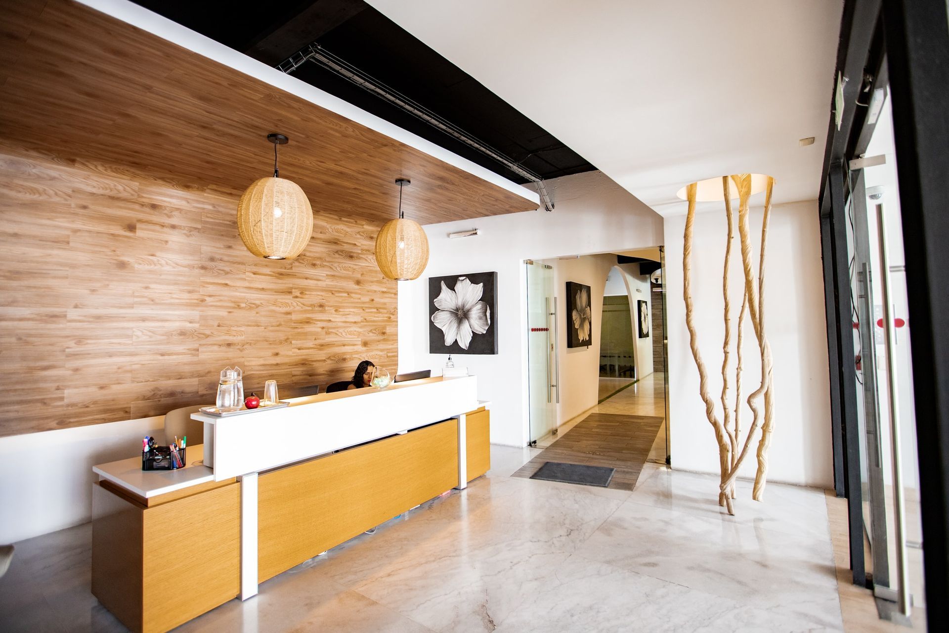 Área de recepción con paneles de madera clara, mostrador de recepción blanco, arte decorativo y grandes ventanales.