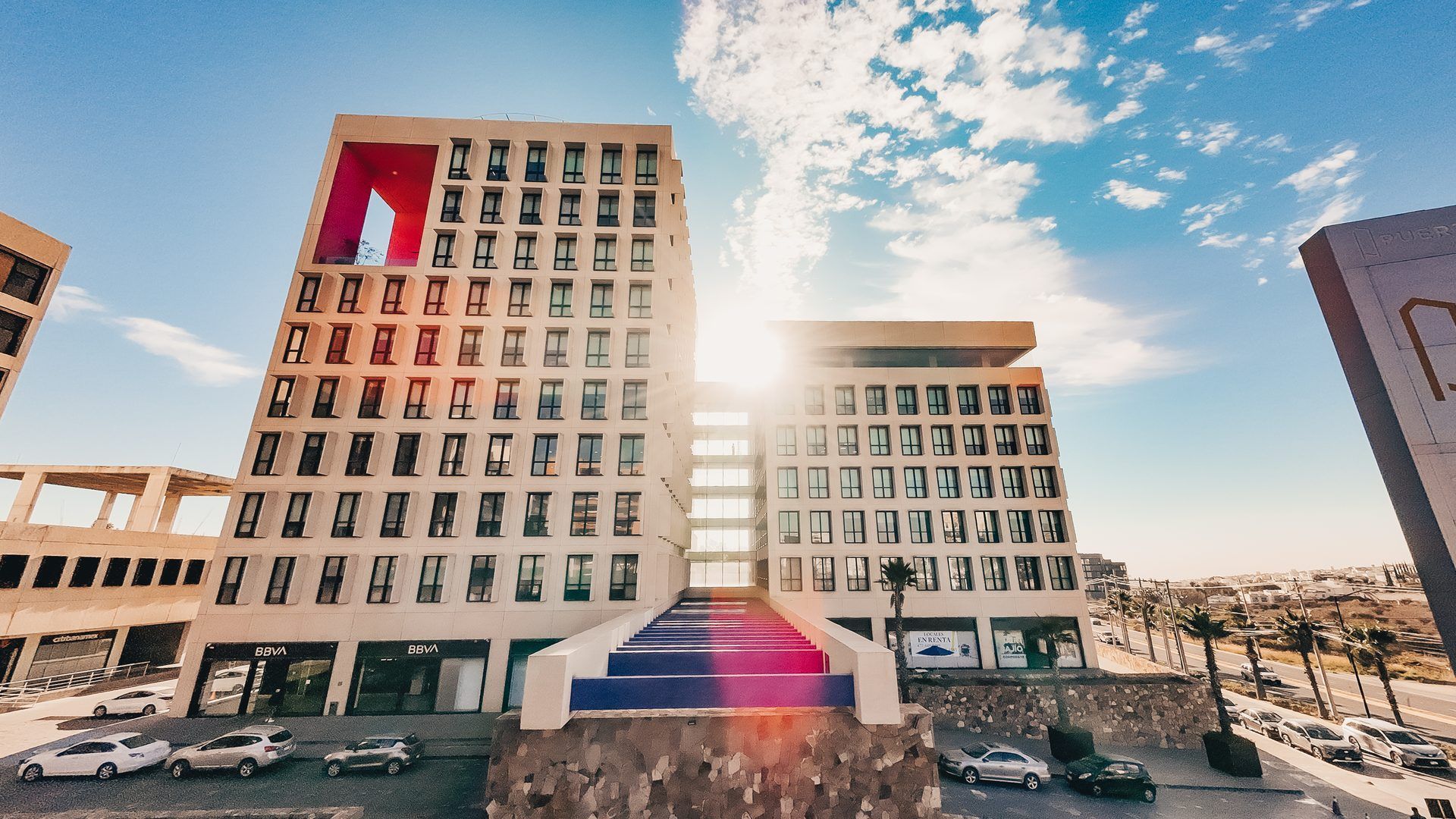 Edificio moderno con sol brillante, cielo azul y coches.