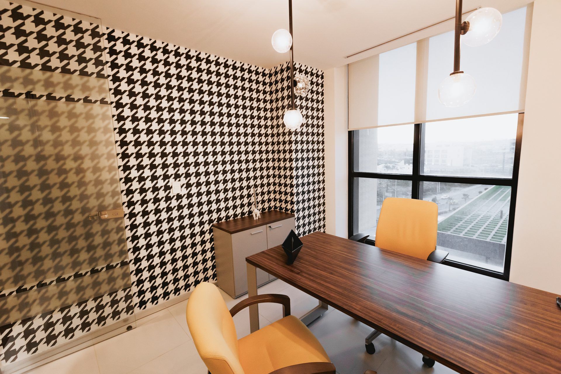 Oficina con papel pintado pata de gallo, un escritorio de madera y dos sillas naranjas.