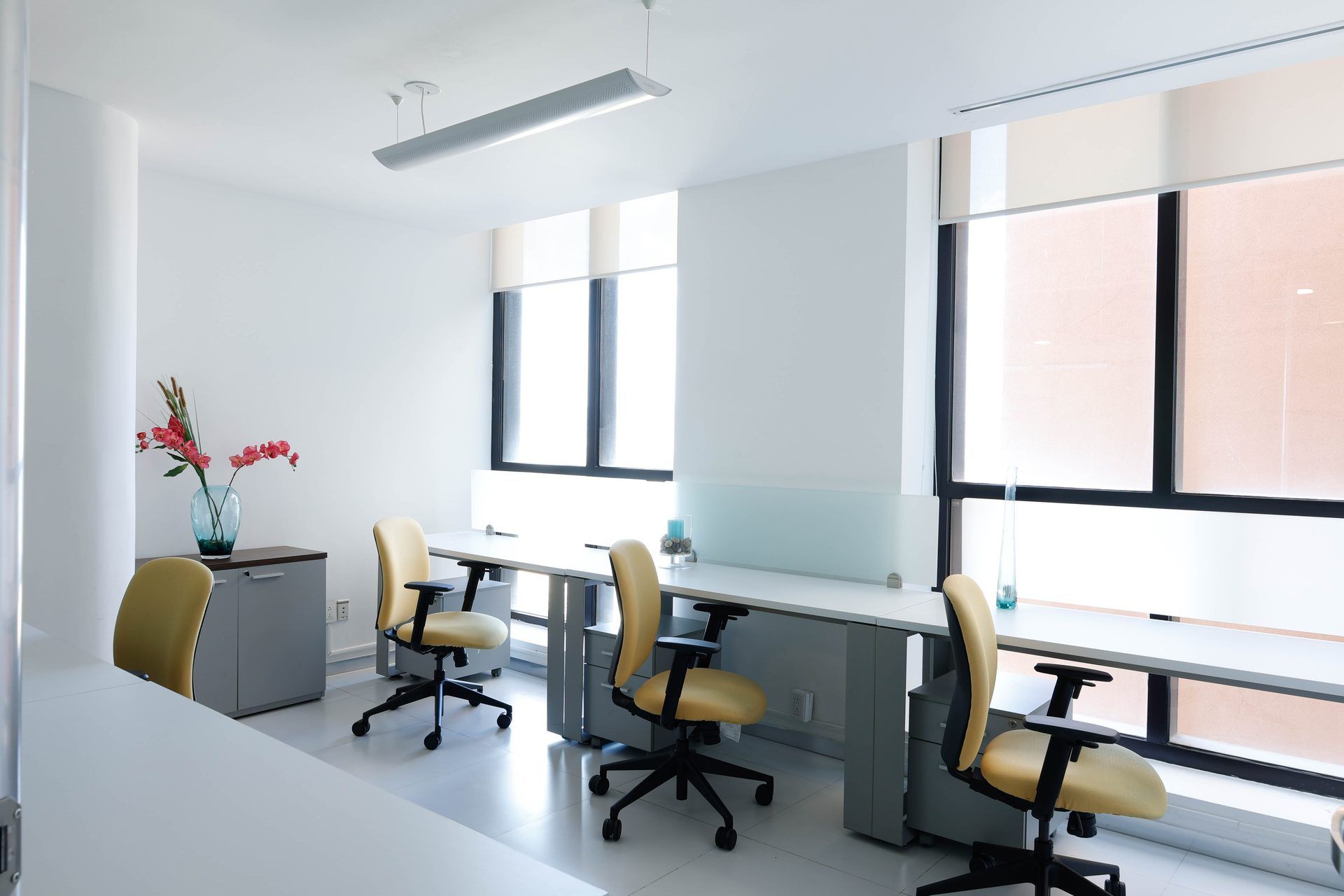 Espacio de oficina moderno con escritorios blancos, sillas beige y grandes ventanas.