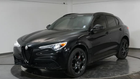 A black alfa romeo stelvio is parked on a display in a showroom.