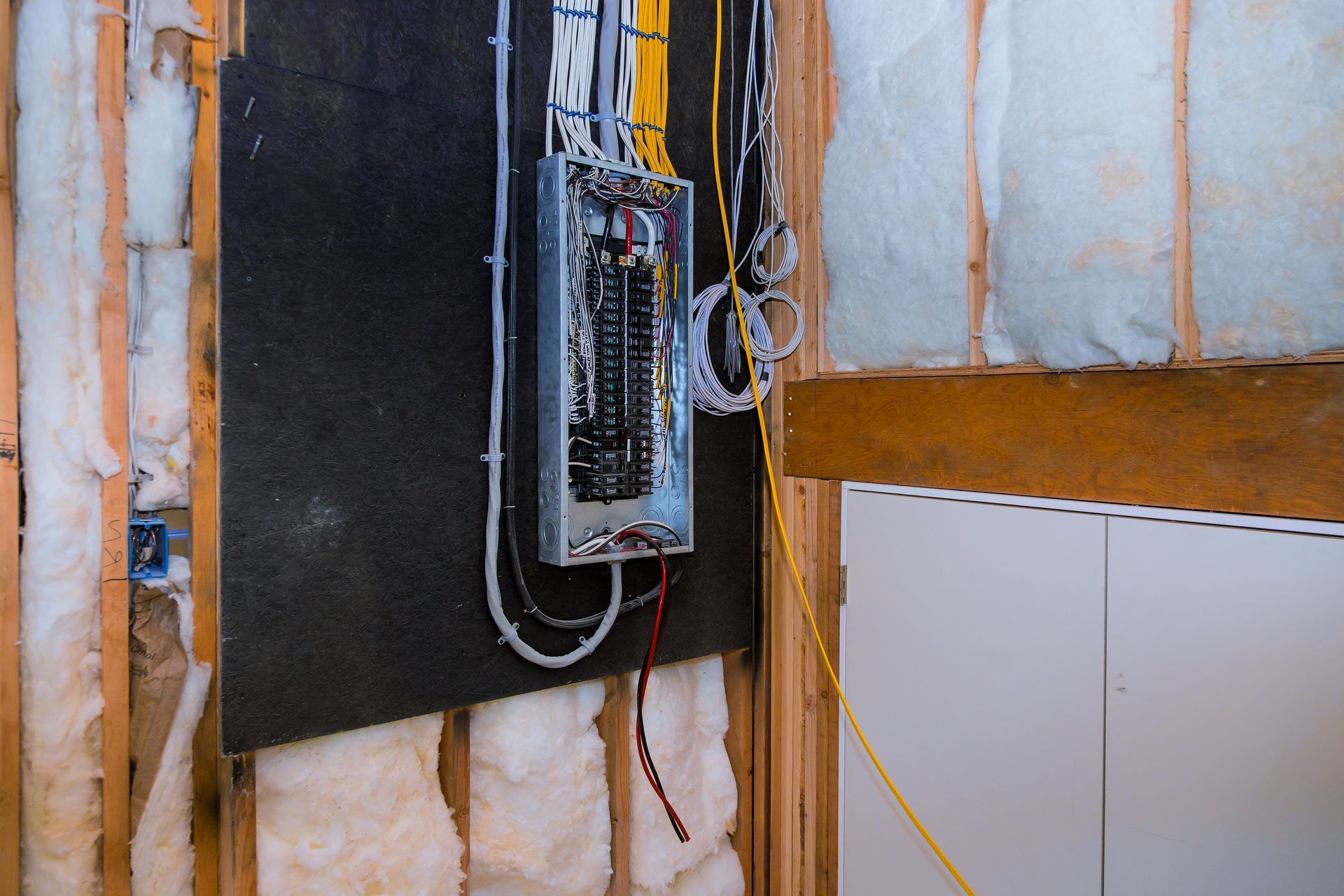 Electrical panel installed in a wooden wall. Wires and breakers visible. Insulation and plywood in the background.
