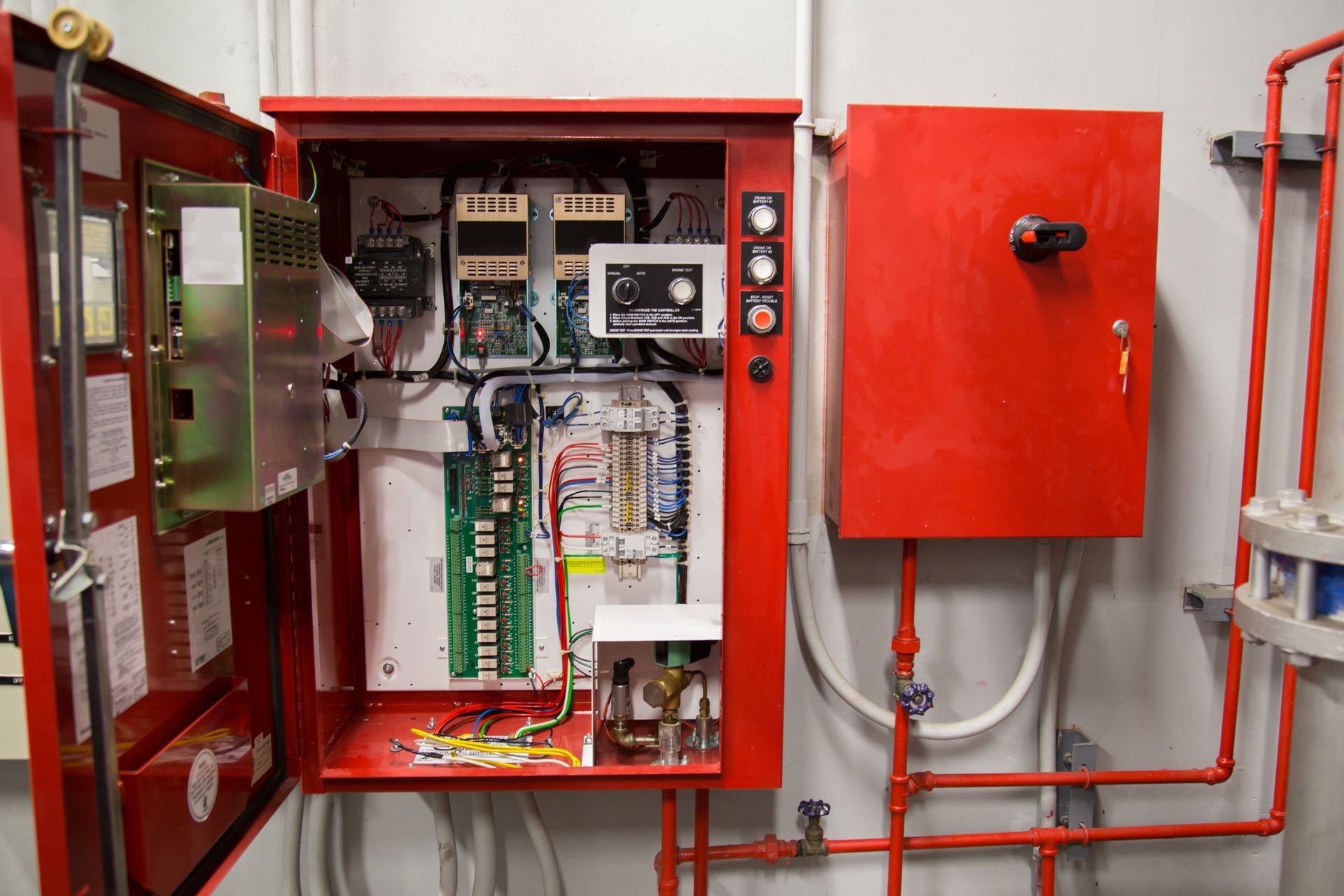 Red electrical panel open, revealing circuits, wires, and a control panel, in a utility room.