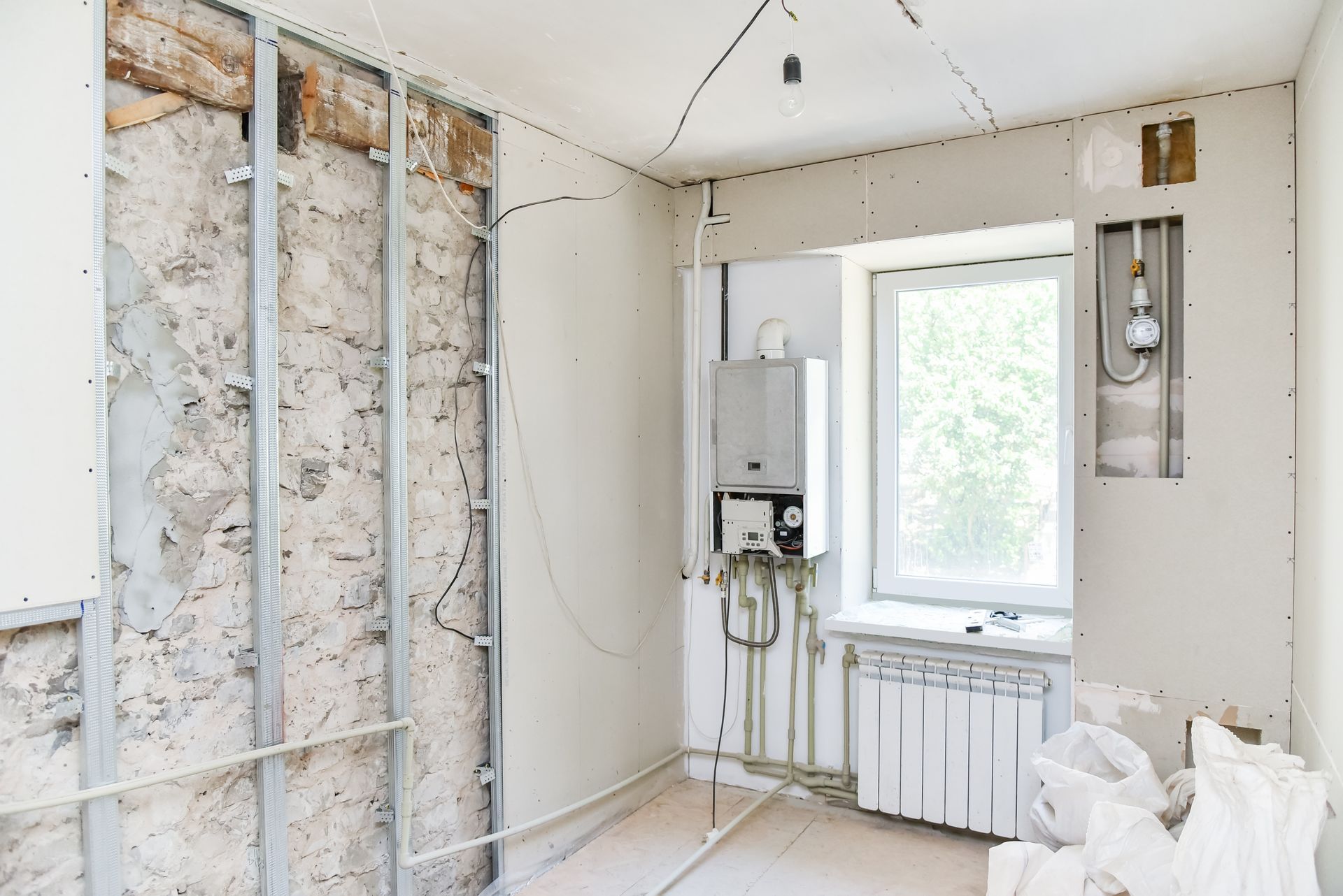 Room under renovation, exposed framing and utilities, drywall partially installed. Window and radiator visible.