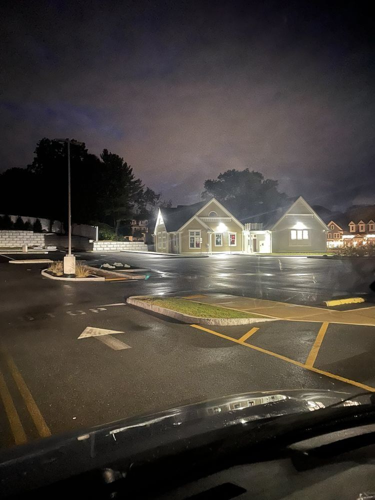 Nighttime view of a building with lit windows, empty parking lot, and cloudy sky.
