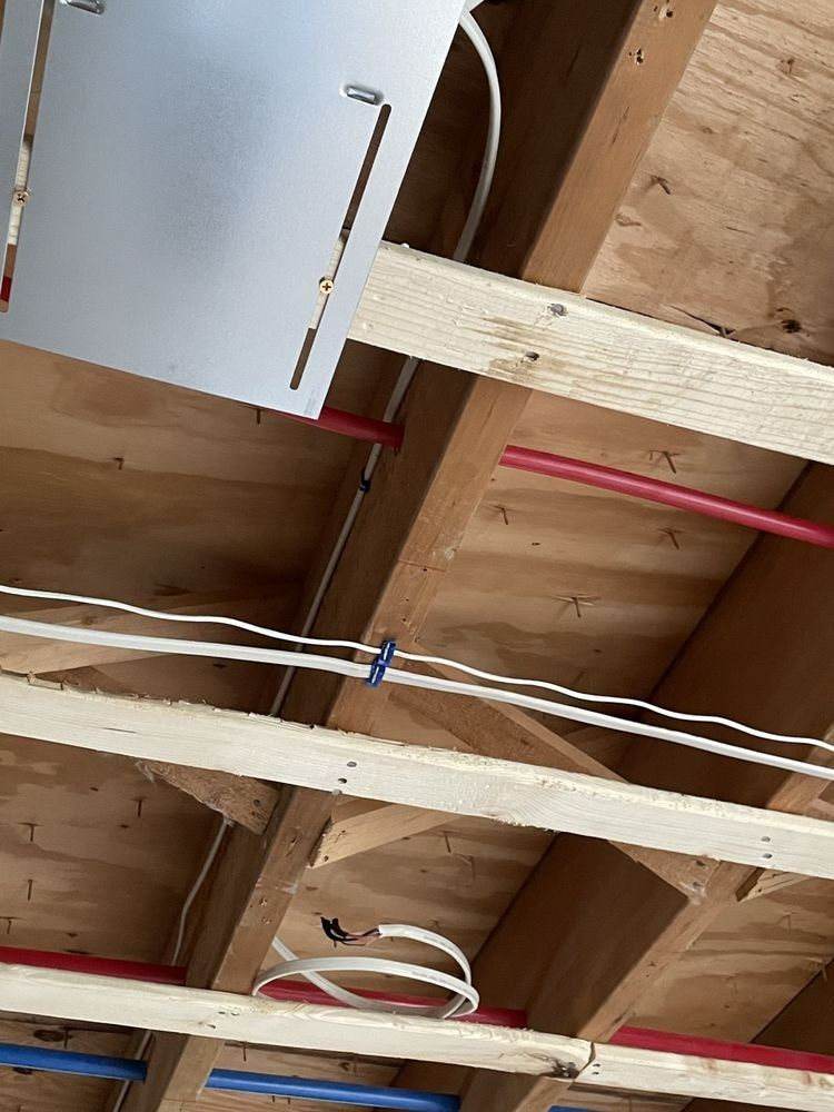 View of wooden floor joists, white electrical wires, and red pipes. A metal plate is fixed to a joist.