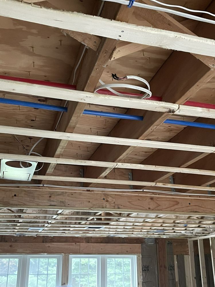 Wooden ceiling joists with exposed plumbing and electrical wiring; room under construction.