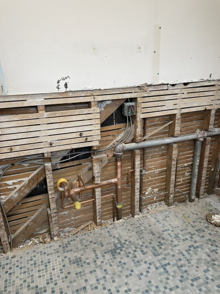 Bathroom wall under renovation, exposed wood framing, plumbing, and electrical.