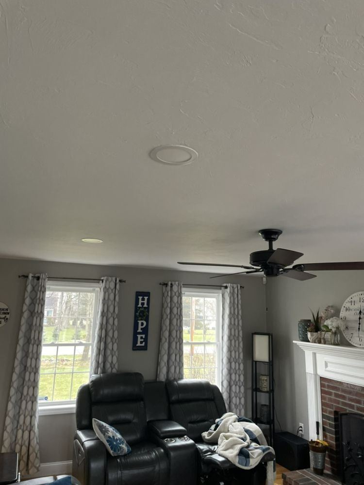 Living room with a black recliner, windows, a ceiling fan, and recessed lighting. A sign reads 