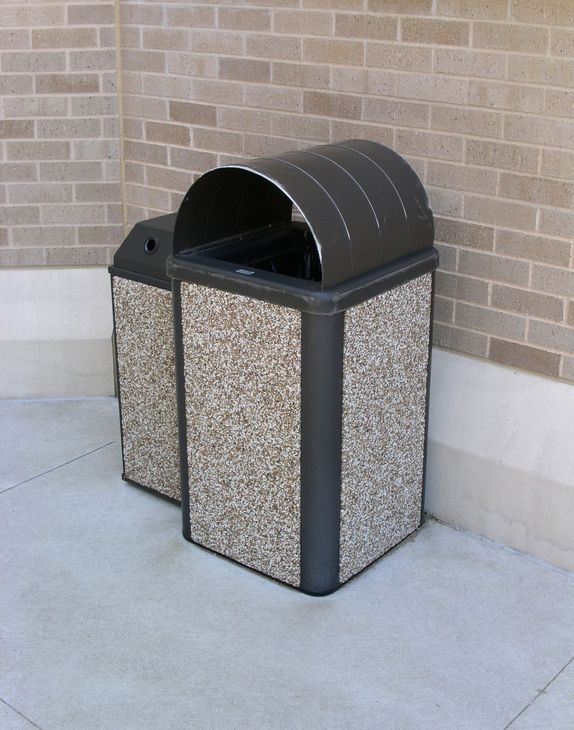 A trash can is sitting on the sidewalk in front of a brick wall