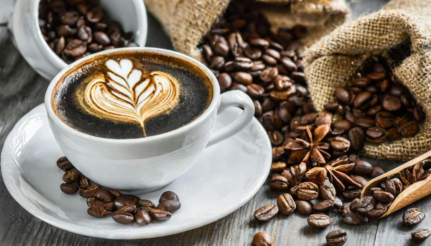 Latte with heart latte art on a white cup, surrounded by coffee beans and cinnamon sticks